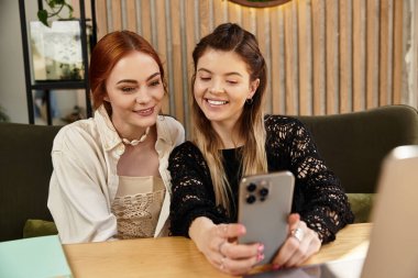 İki genç kadın rahat bir kafe ortamında çalışırken mutlu bir şekilde iş birliği yapıyorlar..