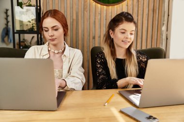 Uzaktan kumandalı bir işte çalışan iki genç kadın şık bir kafede dizüstü bilgisayar kullanıyorlar..