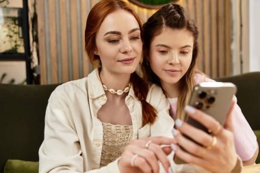 Genç kadınlar, modern bir kafede telefonlarını karıştırırken kahkahalarını paylaşıyorlar..