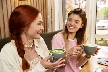 İki genç kadın, modaya uygun bir kafede yeşil içecekleri yudumlarken birbirlerine eşlik etmekten zevk alıyorlar..