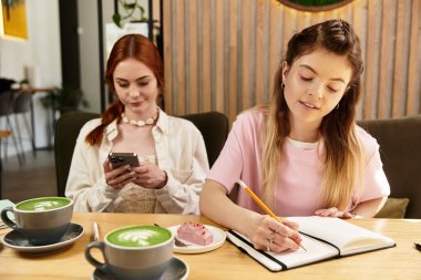 İki arkadaş modern bir kafede vakit geçirmekten keyif alıyor, biri yazarken diğeri de....