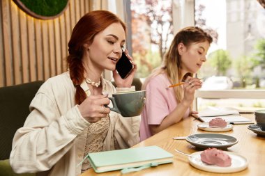 İki genç kadın, modern bir kafede kahvelerini yudumlayarak ve hamur işlerinden zevk alarak sohbet ediyorlar..