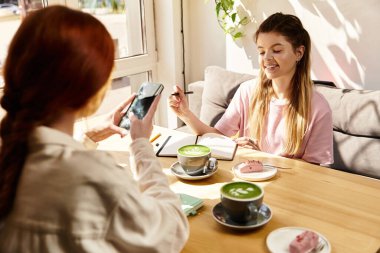 İki genç kadın modern bir kafede birlikte vakit geçiriyorlar, ikramların ve içkilerin tadını çıkarıyorlar..