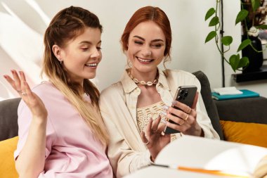 İki arkadaş, modaya uygun bir kafede telefonları kontrol ederken kahkaha ve neşeyi paylaşıyor.