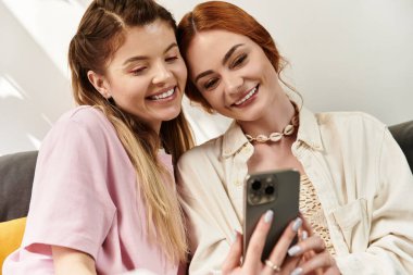 İki genç kadın, modaya uygun bir kafede telefonda eğlenirken kahkahalarını paylaşıyor..