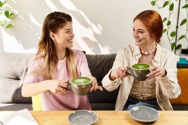 İki arkadaş, modern dekor ve bitkilerle çevrili kahkaha ve yeşil içecekleri paylaşıyor..