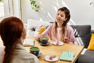 İki arkadaş, şık bir kafede otururken kahkaha ve lezzetli ikramları paylaşıyor..