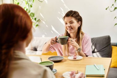 İki genç kadın kahkahalarını ve sohbetlerini içki içerek, rahat bir kafe ortamında geçiriyorlar..