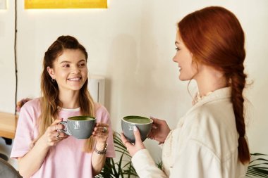 İki genç kadın, modern, şık bir kafe ortamında neşe dolu içkiler paylaşıyorlar..