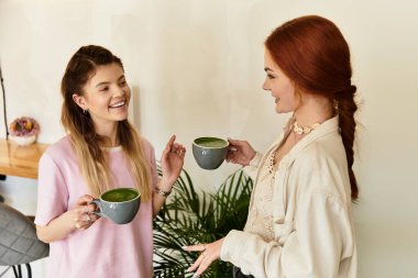 İki genç kadın, davetkar bir kafe atmosferinde bardak tutarken keyifli bir sohbetin tadını çıkarıyorlar..