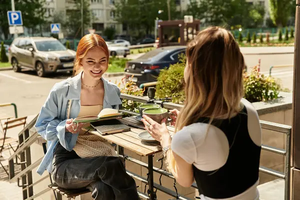İki şık genç kadın, neşeli bir kafede eğlenirken kahkahalarını ve içkilerini paylaşıyorlar..