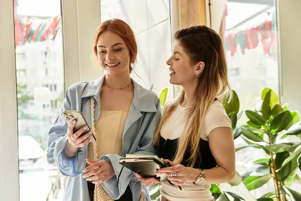 İki genç kadın son moda bir kafede telefonlarıyla kaynaşıyor, neşe ve tarz paylaşıyorlar..