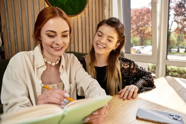 İki genç kadın birlikte okuyorlar, samimi bir kafe ortamında fikir alışverişinde bulunuyorlar..