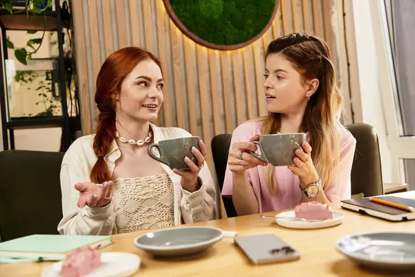 İki genç kadın, şık bir kafede kahve içerken hikayelerini ve kahkahalarını paylaşıyor..