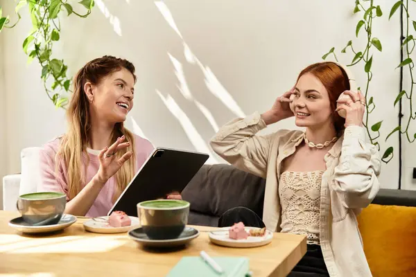 İki genç kadın şık bir kafede keyifli anlar paylaşıyor, ikramlardan ve kahkahalardan birlikte zevk alıyorlar..