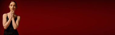 Çekici genç bir kadın şık siyah bir elbise içinde poz veriyor, kırmızı, afişe karşı sofistike bir şekilde poz veriyor.