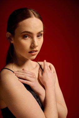 Kendine güvenen genç bir kadın şık siyah bir elbise içinde canlı kırmızı renge karşı zarifçe poz verir..