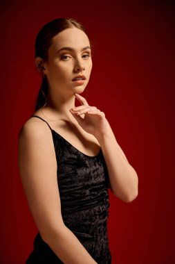 Güzel genç bir kadın zarif bir şekilde poz verir, siyah bir elbiseyle stilini ve özgüvenini gösterir..