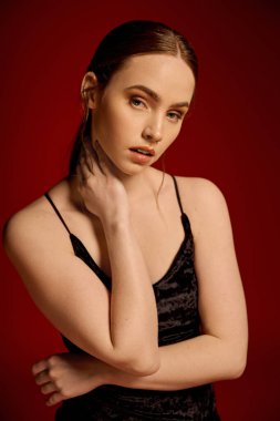 Çekici, siyah elbiseli genç bir kadın, kırmızı bir arka planda zarafet sergiliyor..