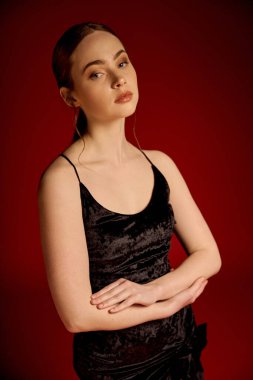 Genç bir kadın kendine güveni tam olarak siyah bir elbise içinde duruyor. Zarafet ve duruş sergiliyor..