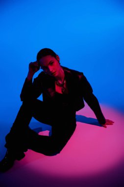 Güzel genç bir kadın şık bir şekilde poz verir. Pembe ve mavi ışıklarla aydınlatılır..