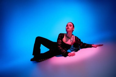 Güzel genç bir kadın zarif bir şekilde poz verir. Pembe ve mavi ışıkla aydınlatılır..