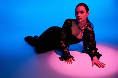 Pembe ve mavi ışıkta yatmış, şık kıyafetli genç bir kadın yerde yatar..