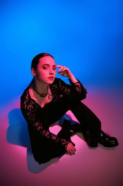 Şık genç bir kadın parlak mavi bir arka plan önünde pembe ışıklandırmayla poz veriyor..