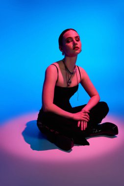 Güzel genç bir kadın zarif bir şekilde pembe ve mavi ışıklarla aydınlatılmış şık bir elbisenin içinde oturuyor..