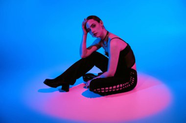 Güzel genç bir kadın zarif bir şekilde pembe ve mavi ışıklarla aydınlatılmış şık bir elbiseyle uzanır..