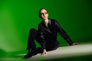 Tarz sahibi genç bir kadın, modern modada yeşil bir zemine karşı güvenle poz verir..