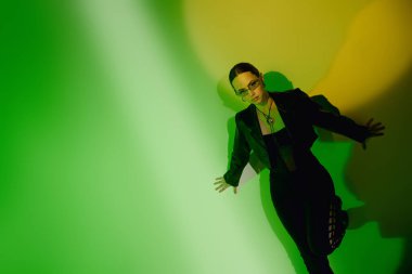 Gösterişli siyah elbiseli genç bir kadın canlı yeşil bir arka plana karşı güvenle poz verir..