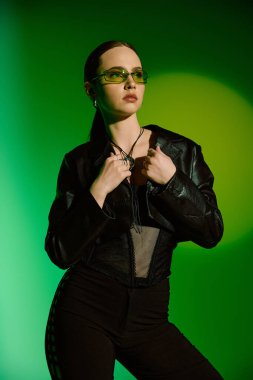 Kendine güveni olan genç bir kadın, fevkalade yeşil arka planlı, şık bir siyah elbiseyle poz veriyor..