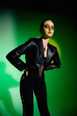 Tarz sahibi genç bir kadın, yeşil bir arkaplan karşısında modaya uygun bir siyah elbise modelliyor..