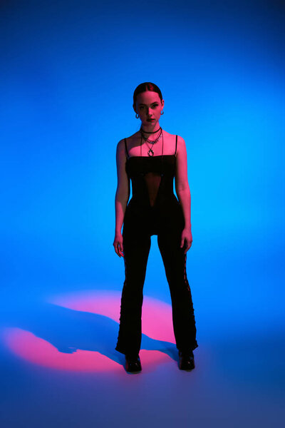 A beautiful young woman stands confidently against a vivid blue backdrop, styled elegantly.