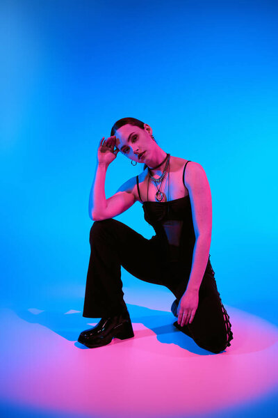Stylish young woman poses gracefully with pink lighting against a blue backdrop.
