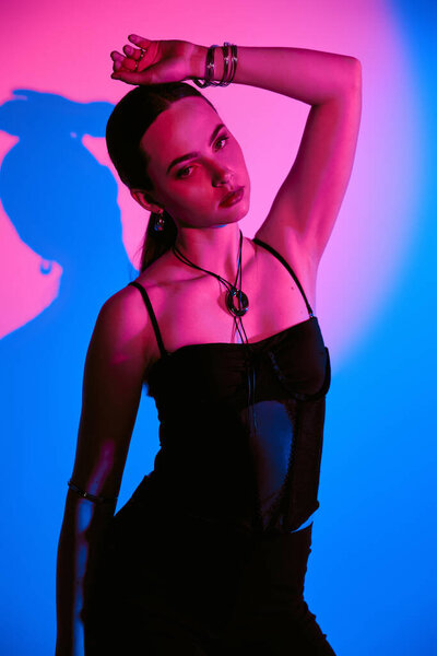 A beautiful young woman poses confidently in a trendy outfit with striking pink lighting.