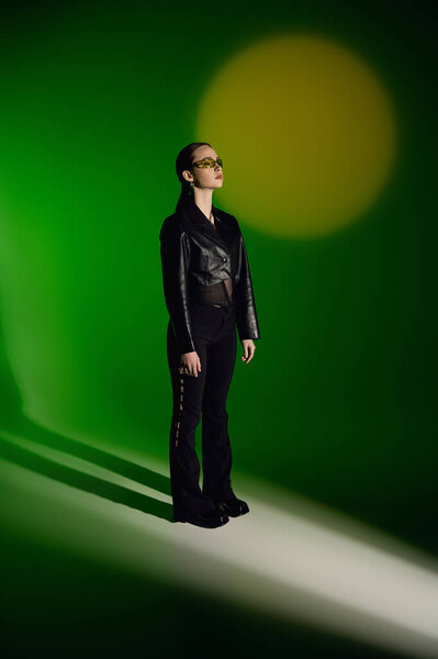 Красивая молодая женщина уверенно позирует в шикарном черном наряде на ярком зеленом фоне.