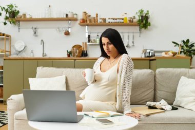 Genç hamile bir kadın bir fincan çayla kanepede dinleniyor ve sıcak bir video görüşmesi yapıyor..