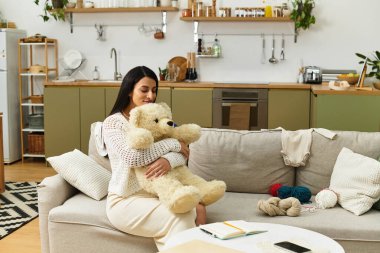 Güzel genç bir kadın evdeki kanepesinde dinlenirken oyuncak ayıya nazikçe sarılıyor..