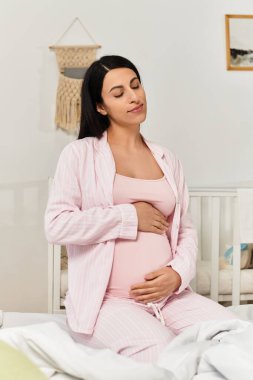 Pembe pijamalı genç bir kadın yatağında oturmuş beklerken huzurlu bir anın tadını çıkarıyor..
