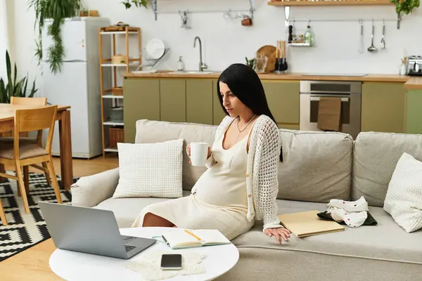 Genç bir kadın şık evinde bir kanepede dinleniyor, hamileyken sıcak bir içkinin tadını çıkarıyor..