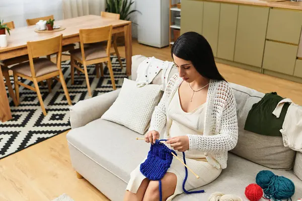 Modern bir oturma odasında ustalıkla örgü örüp hamileliğinin tadını çıkaran genç ve güzel bir kadın..