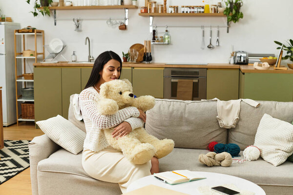 Красивая молодая женщина нежно обнимает плюшевого мишку, расслабляясь дома на диване..
