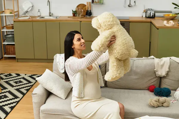 Neşeli hamile bir kadın elinde oyuncak ayıyla gülümsüyor..