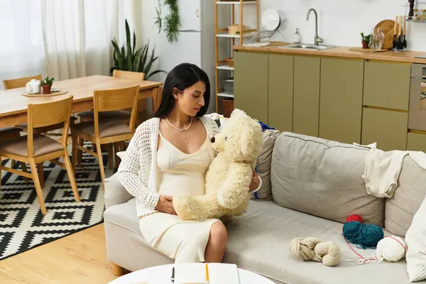 Bekleyen anne koltukta rahat bir şekilde oturur, sıcak, davetkar bir yerde oyuncak ayıyı kucaklar..