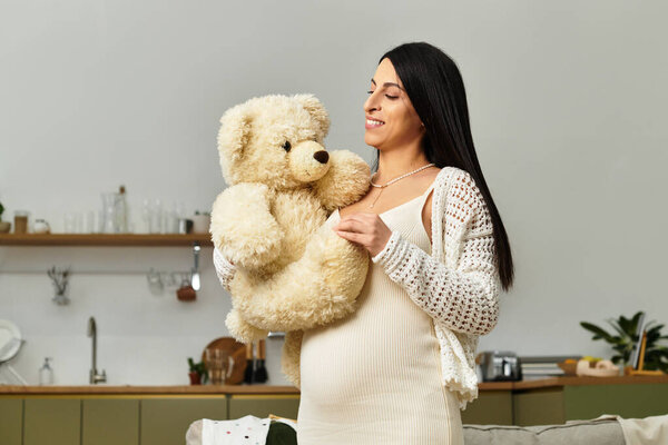 Молодая женщина колышет большого плюшевого мишку, обнимая свою беременность в спокойной домашней обстановке.