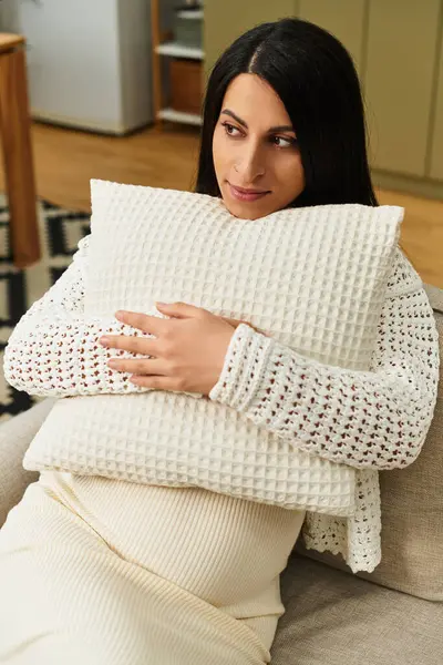 Güzel hamile bir kadın koltukta oturur, rahatlarken yumuşak bir yastığa sarılır..