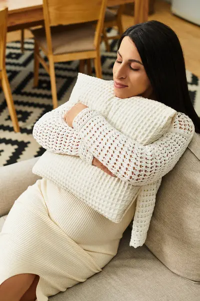 Güzel genç bir kadın, neşeli bir şekilde yumuşak bir yastığa yaslanır ve hamileliğinin değerli anlarından zevk alır..