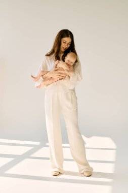 Sevimli genç bir anne çocuğunu nazikçe kucağına alır. Parlak güneş ışığında sıcaklığı ve şefkati yayar..